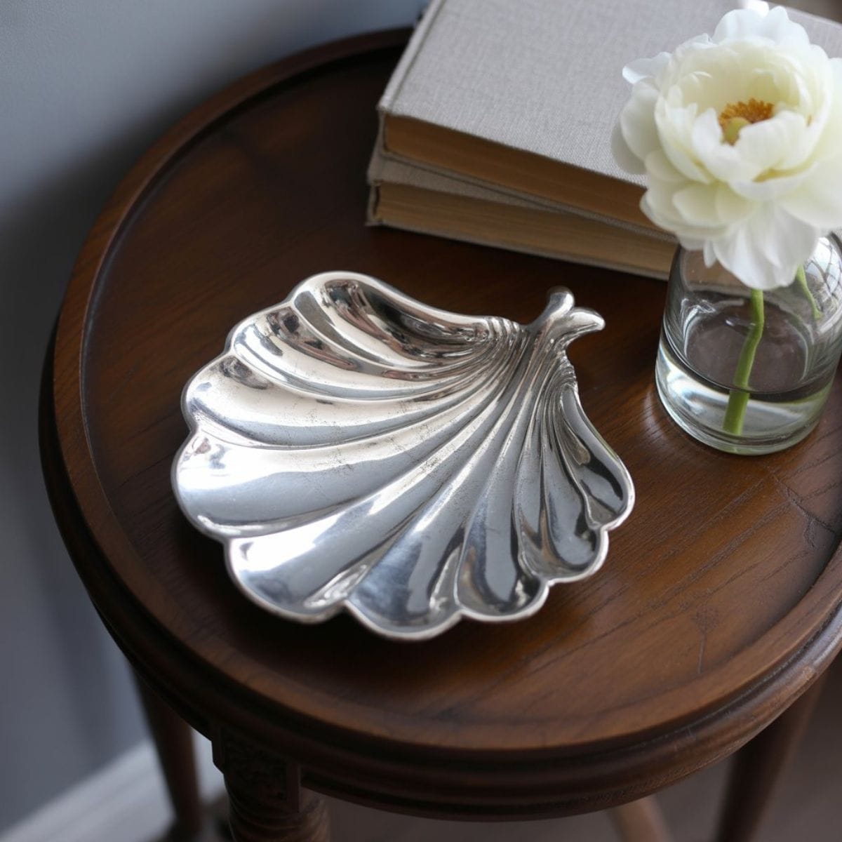 An antique silver shell-shaped dish with a soft patina sitting on a dark wood side table, illustrating effortless elegance and quiet luxury decor.